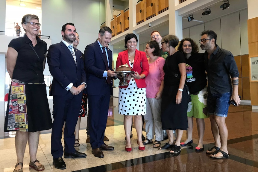 Parliamentarians and members of the public gather around the cake.