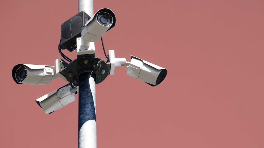 Four security cameras on a pole against a pink background.