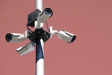 Four security cameras on a pole against a pink background.