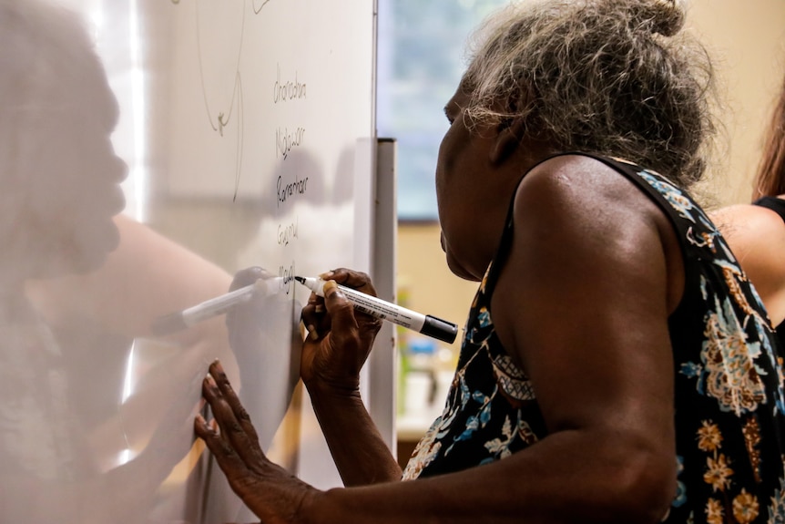 Glenda Gondjalk writes on a whiteboard. She has grey hair.