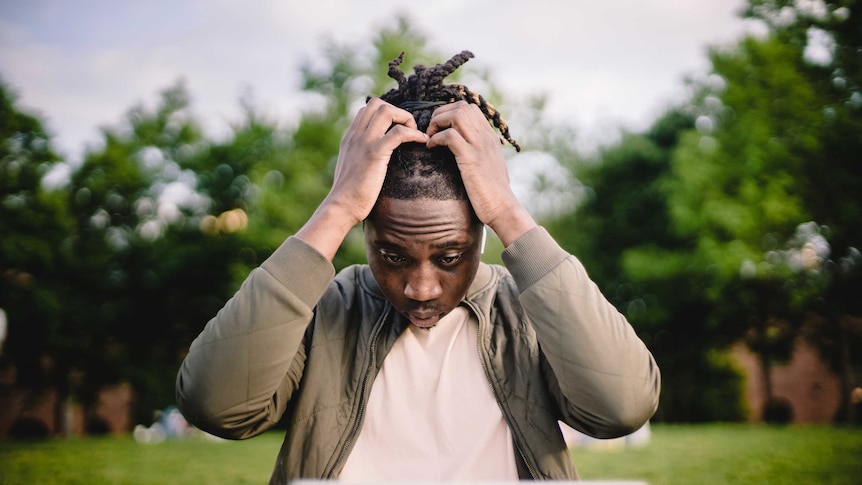 Man holds his head while looking at a laptop computer, for a story about taking mental health breaks when working from home.