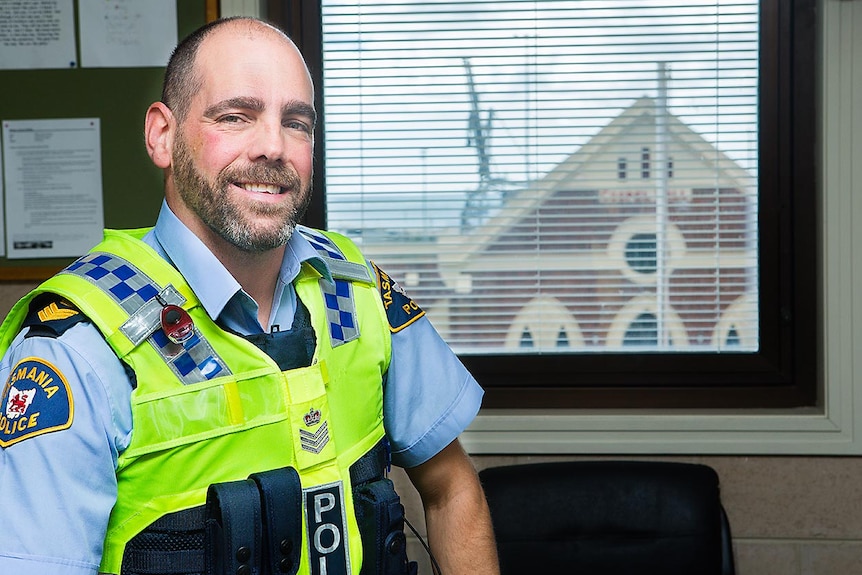 A policeman with a beard sitting in front of a window.