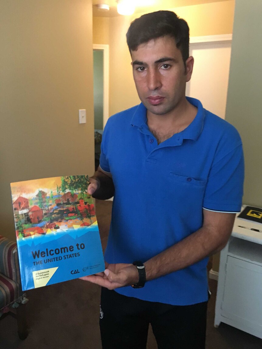 A man in a blue shirt holds up a book titled Welcome to the United States.