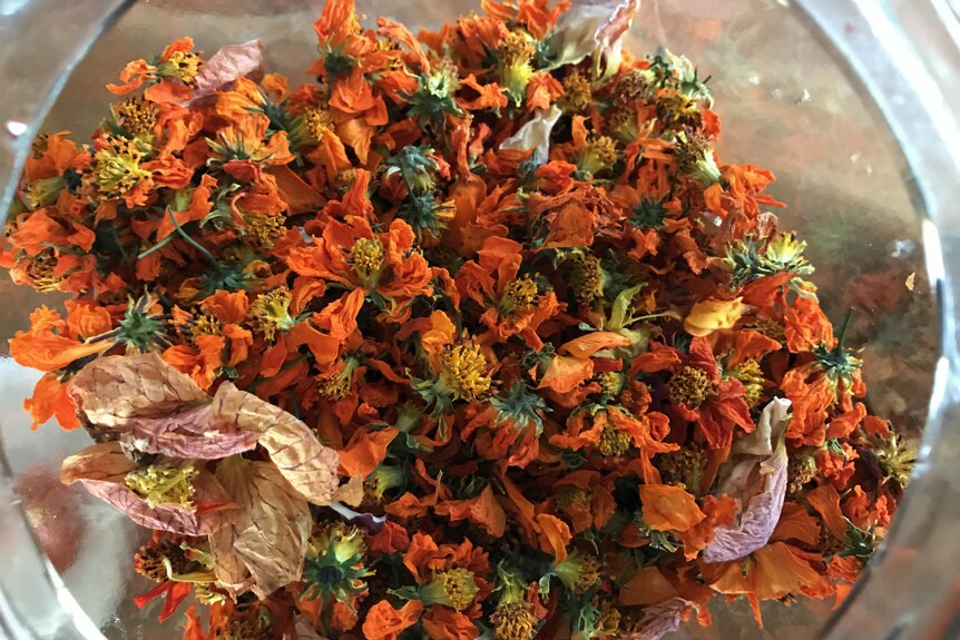 Bright orange dried marigolds and pink dried rose petals in a jar.