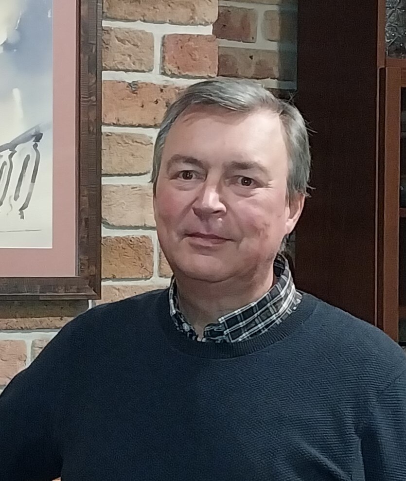 A close crop of an older man standing in front of a brick wall