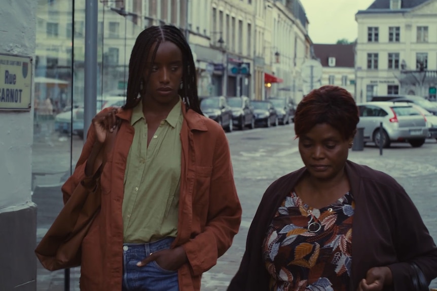 Two African women walk down a street in a French city, talking.