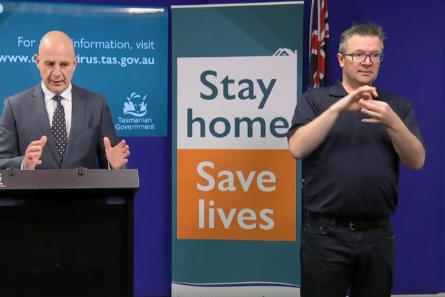 Interpreter doing sign language while standing next to Tasmania premier standing at lectern.