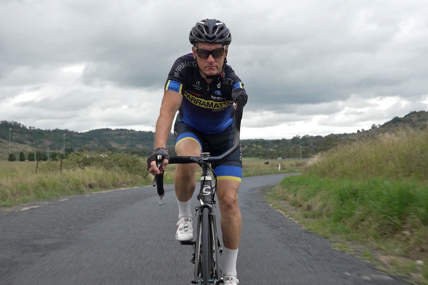 A man in cycling attire rides a racing bike on a country road.