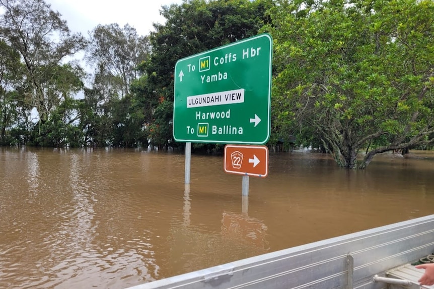 A green road sign in brown water with a tinny in the foreground