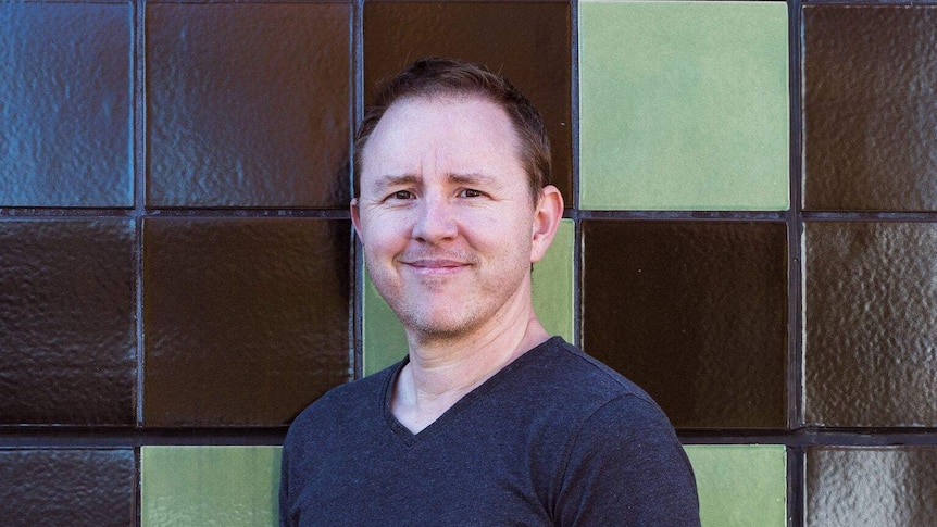 A man standing in front of a tiled wall.