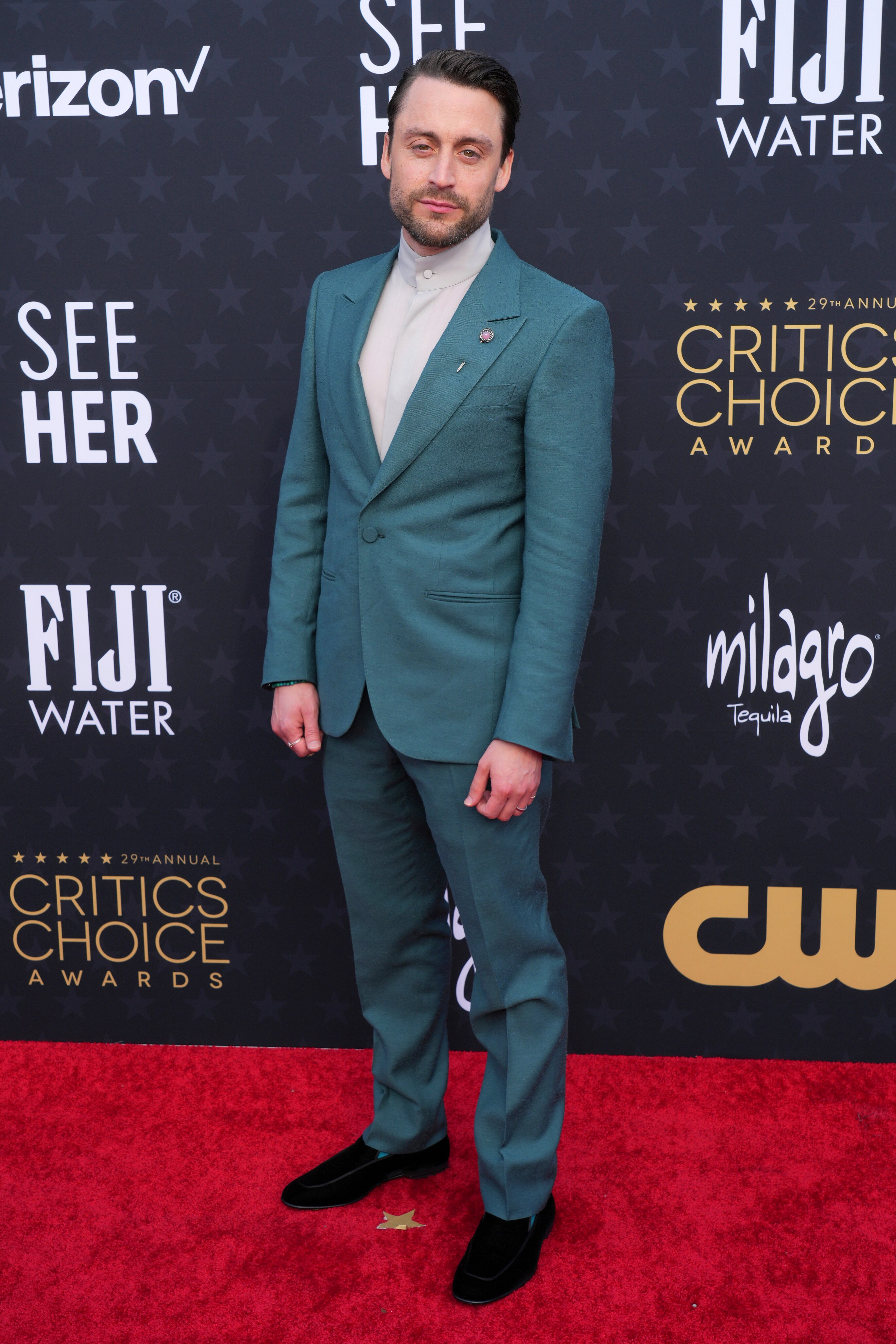 Kieran Culkin portant un costume bleu sarcelle avec une chemise boutonnée grise à col haut en dessous