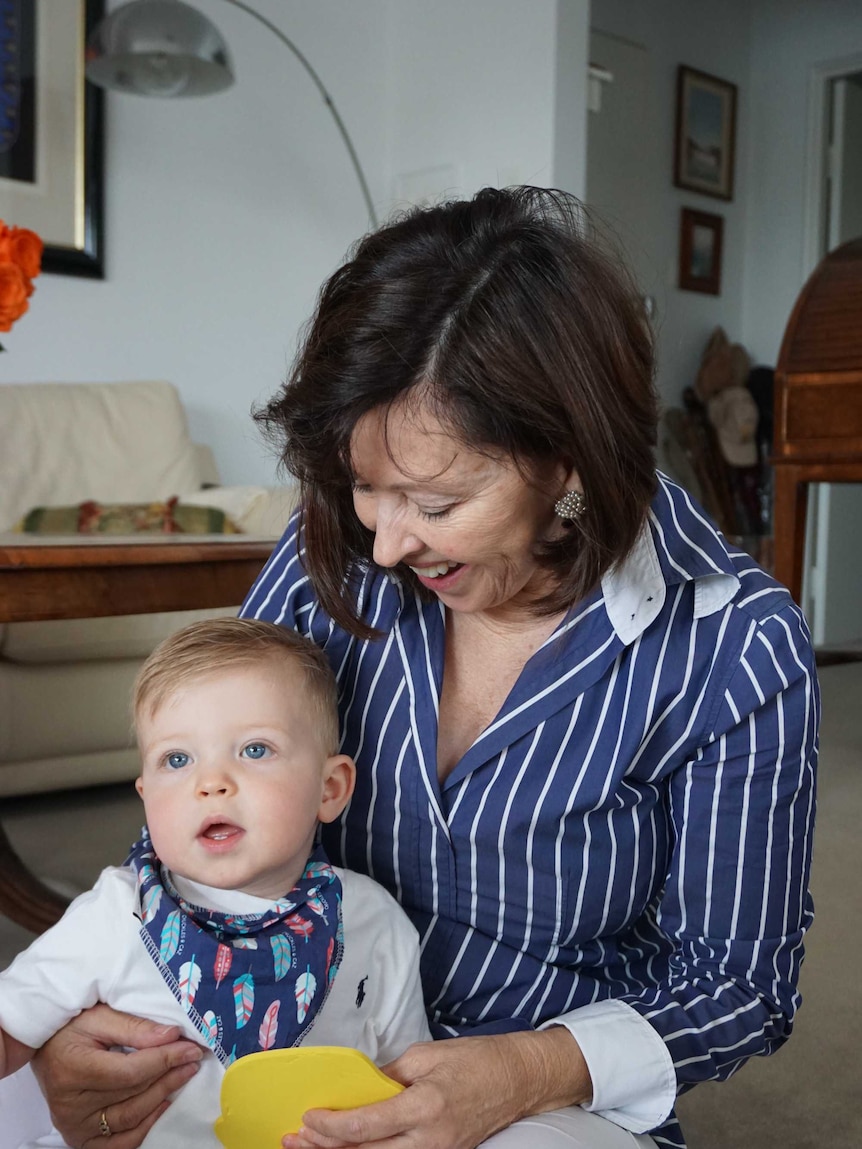 Judi Green in blue-and-white shirt, holding grandchild who's looking slightly left of camera.