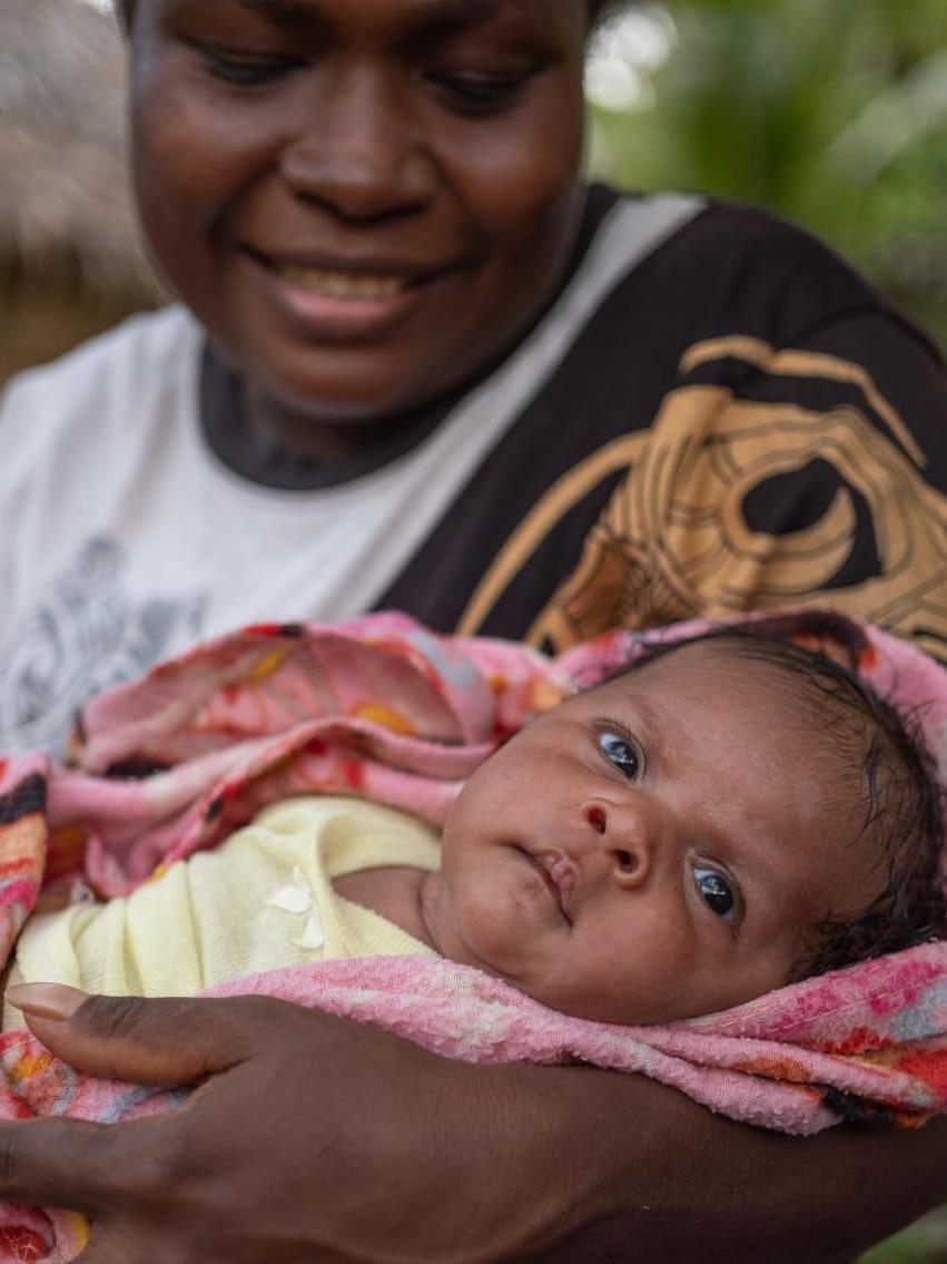 A woman in Vanuatu smiles as she holds her baby daughter.