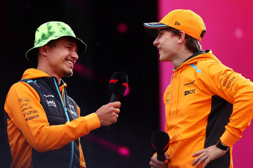 Two McLaren F1 drivers smile as they stand on a stage with microphones during a talk for fans at the British grand prix.