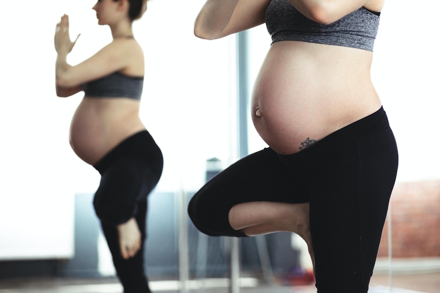 Pregnant woman doing yoga in front of mirror.
