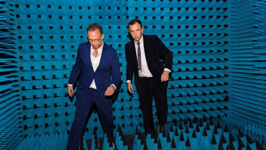 The two members of Soulwax wear suits inside a blue room with spikes on every surface