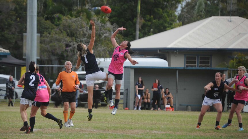 Two women's AFL players jump for the ball in a ruck contest.