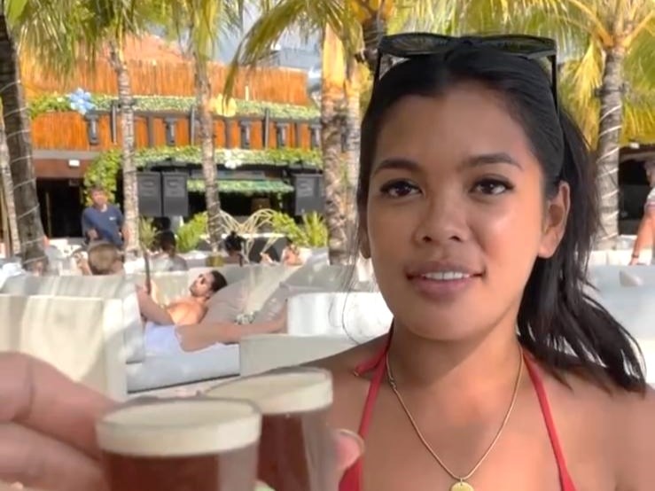 A woman in bikini holding shots smiling to camera.
