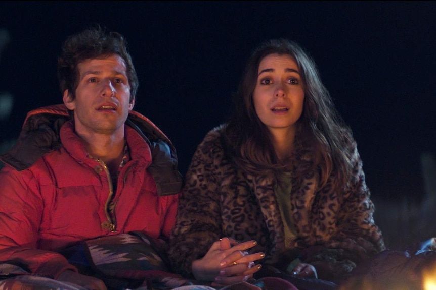 Andy Samberg and Cristin Milioti sitting in front of a campfire in Palm Springs