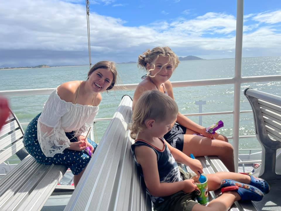 Two older girls and a younger boy are smiling together on a boat.