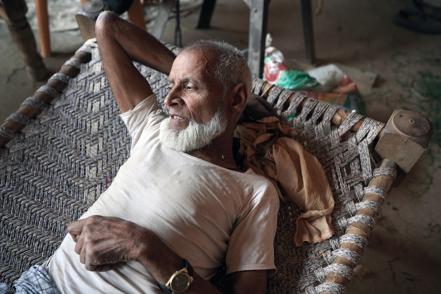 A man with a grey beard lays on a straw bed.