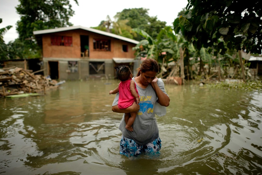 A woman and child leave a flood submerged house in Macapagal, north of Manila