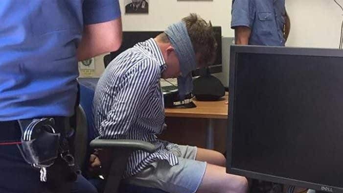 A man in a striped shirt handcuffed and blindfolded