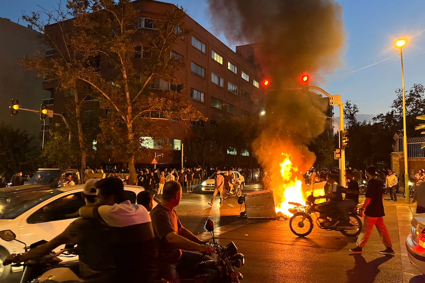 A police motorcycle and a trash bin are burning during a protest.