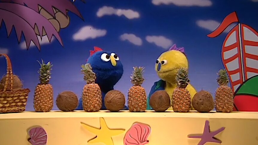 Puppet characters look at row of pineapples and coconuts