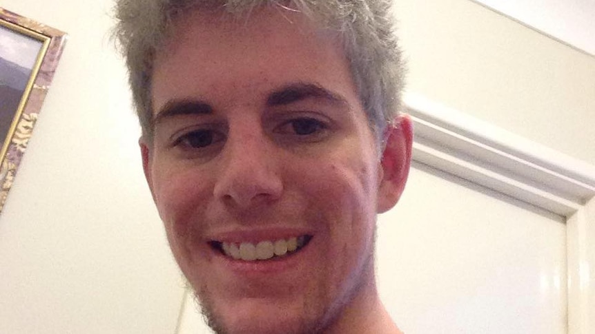 a selfie of a man smiling and looking down at the camera in front of a cream wall 