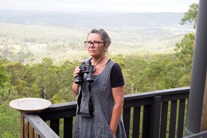 woman stands with binoculars on hill standing on verandah