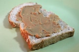 A slice of bread with peanut butter spread across it sits on a green table.