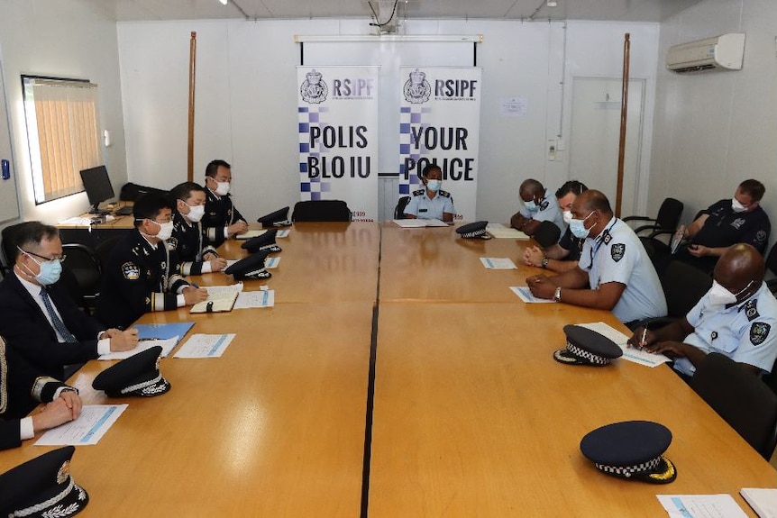 身穿制服的男子围坐在一张长桌旁，背景中可以看到警察的横幅。