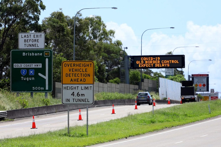 Traffic on motorway off-ramp with COVID-19 checkpoint signs at Queensland-NSW border at Coolangatta.