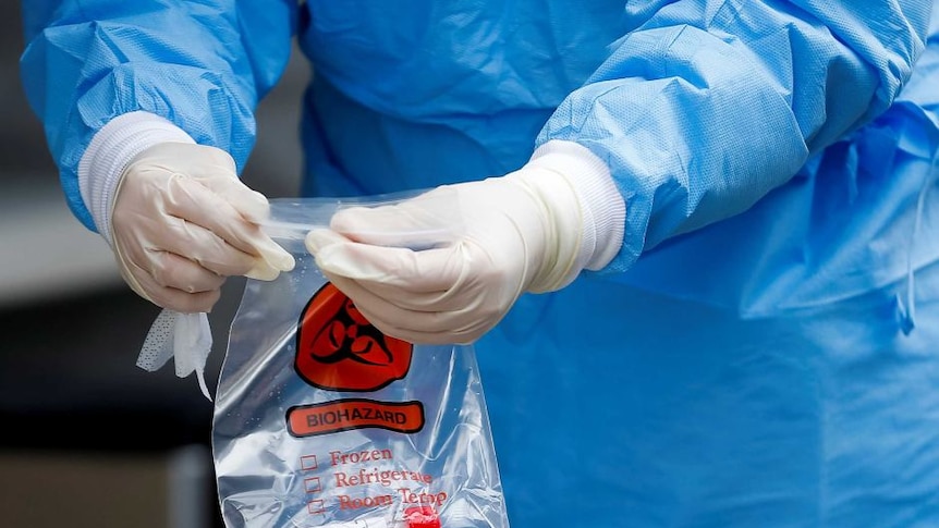 A doctor with gloves and PPE gear carries a coronavirus test.