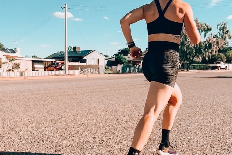 A woman in the middle of a running stride on an outback road.