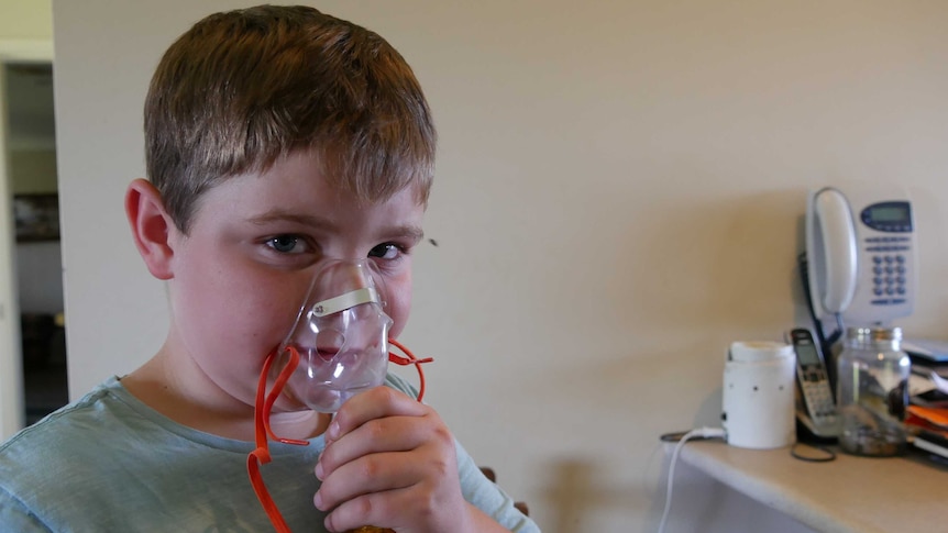 Lincon stands at kitchen counter with breathing mask over his face