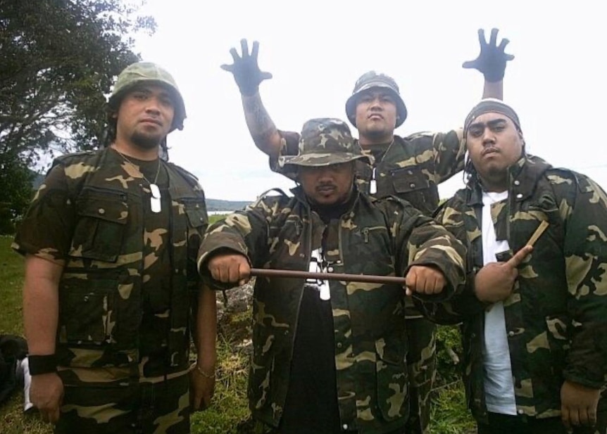 Four Polynesian men dressed in army uniform stare at camera. Surrounded by green bushland. 