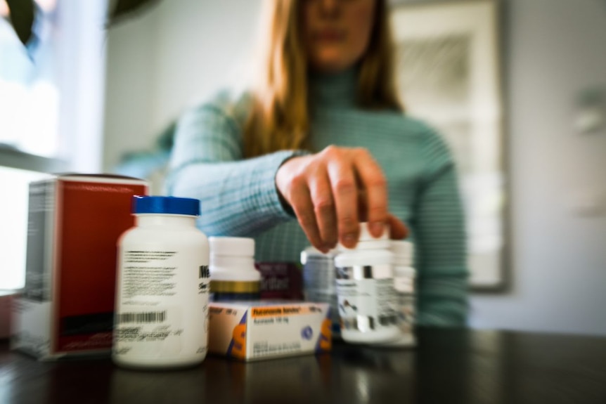 A woman is seen blurred behind a pile of different medicines
