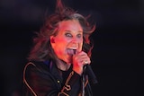 Ozzy Osbourne singing into microphone on stage.