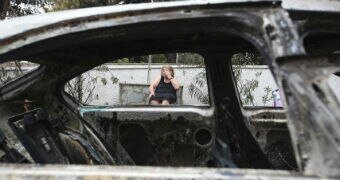 A woman looks on amid burned cars in Mati, Greece after a fire.
