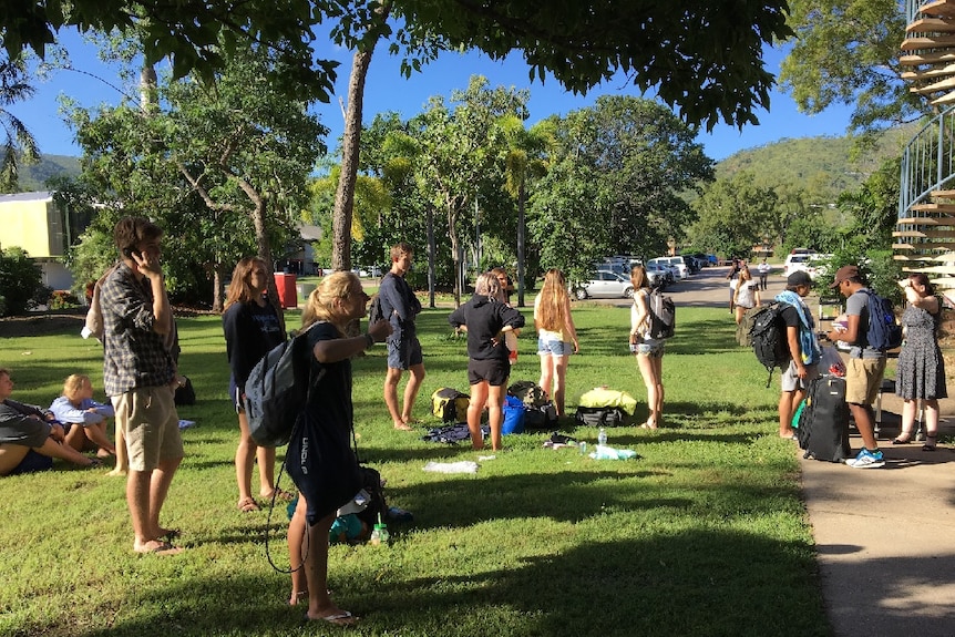 Students stand with belongings on grass outside their burnt residence.