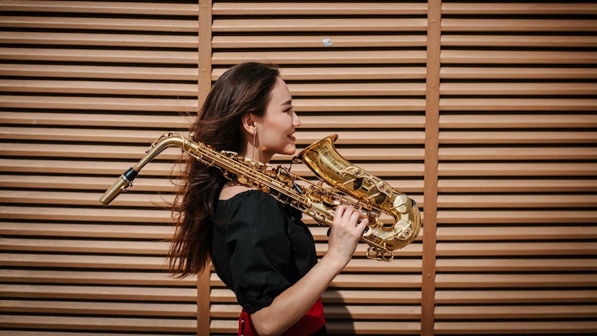 A woman holds her saxophone over her shoulder