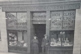 A black and white photo of an old confectionary store with two people standing at the entrance.