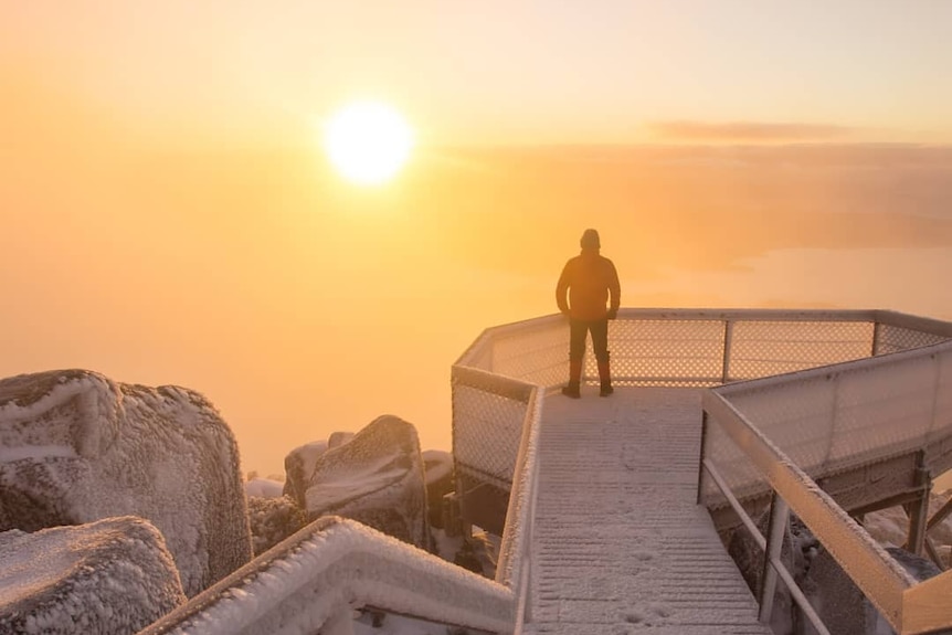 Person viewing sunrise from mountain viewing platform in icy conditions.