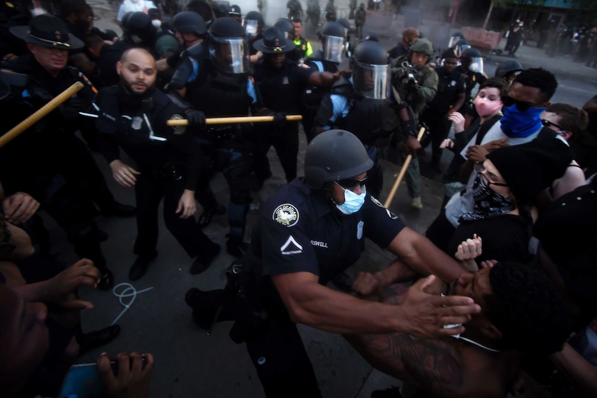 About 50 people, a mix of police and protesters, clash in a street, with a black police officer putting his hands on a black man