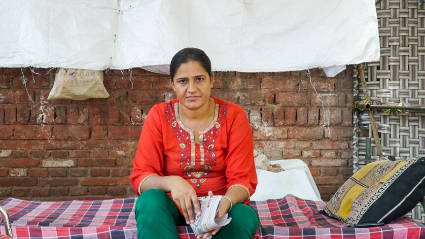 A woman sits on a pallet bed holding a newspaper