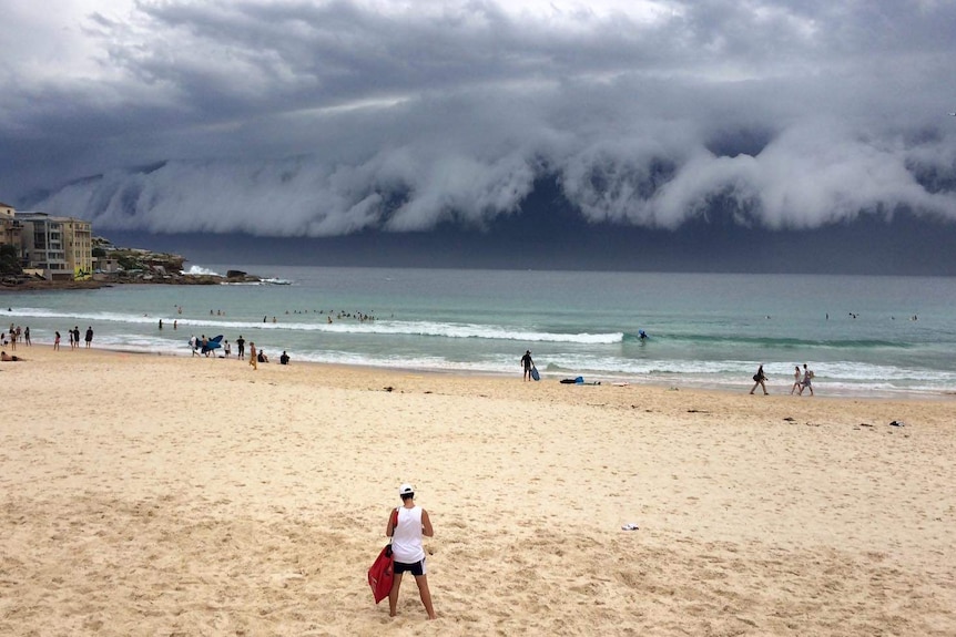 People go about their day on Bondi Beach in Sydney as a storm front moves towards the city.