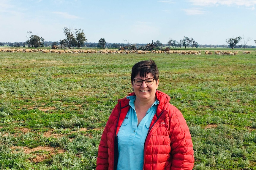 A smiling woman in a red coat standing in a green paddock.