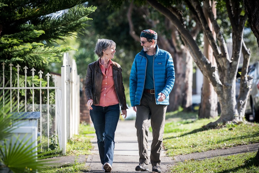 Karl Schurr and Annie McCluskey look at each other while walking down a tree-lined footpath.